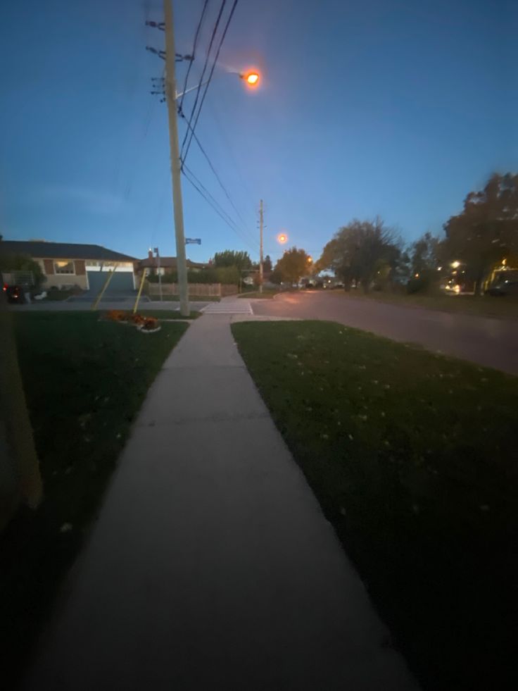 an empty sidewalk at night with street lights in the background