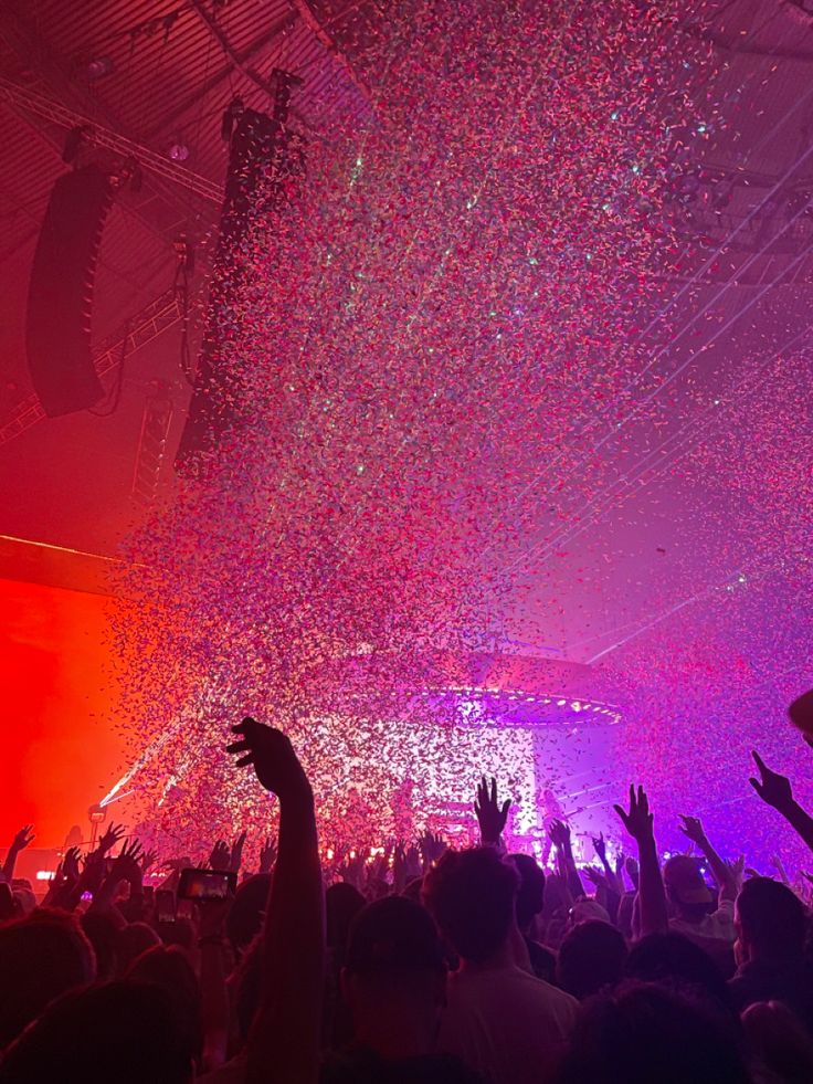 a crowd at a concert with confetti falling from the ceiling and hands in the air