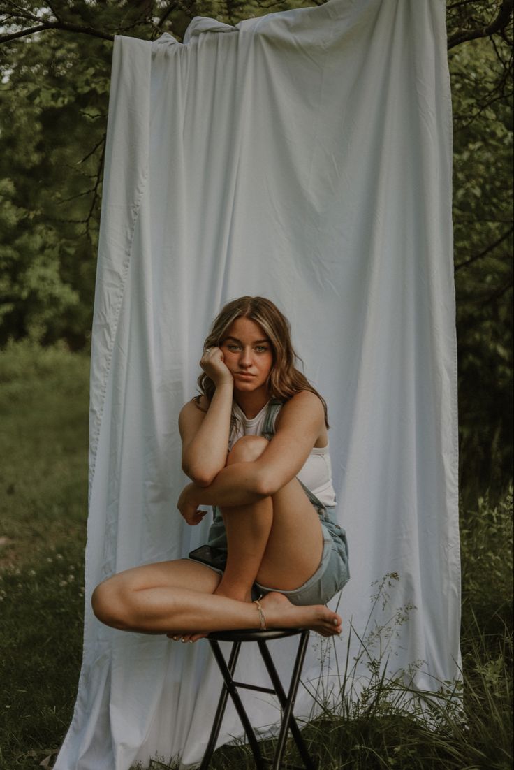 a woman sitting on top of a chair next to a white curtain