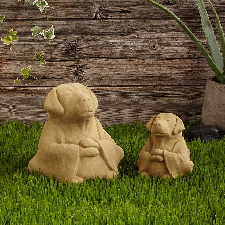 two clay dogs sitting in the grass next to a potted plant