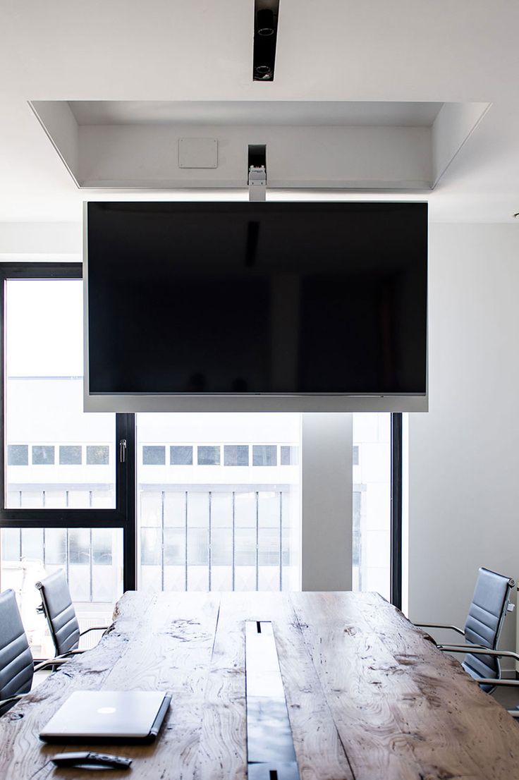 an empty conference room with a flat screen tv above the table and laptops on the desk