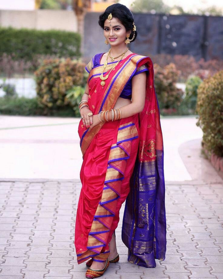 a woman in a red and blue sari is standing on the sidewalk with her arms crossed