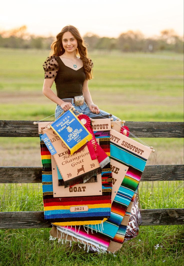 a woman sitting on top of a pile of books in front of a wooden fence