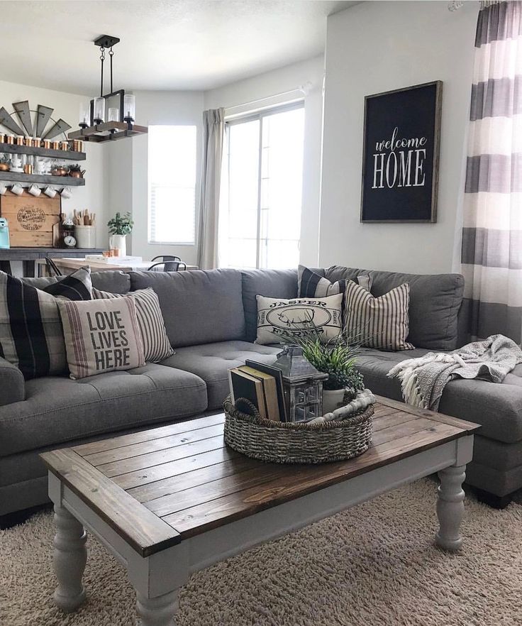 a living room with gray couches and pillows on top of the coffee table in front of a window