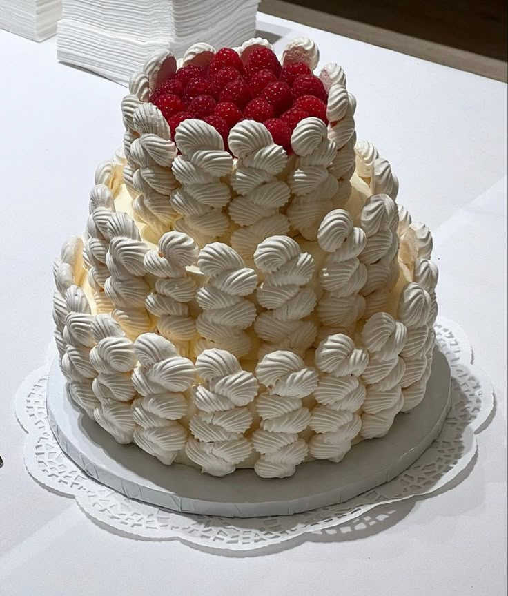 a three tiered cake with white icing and raspberries on the top