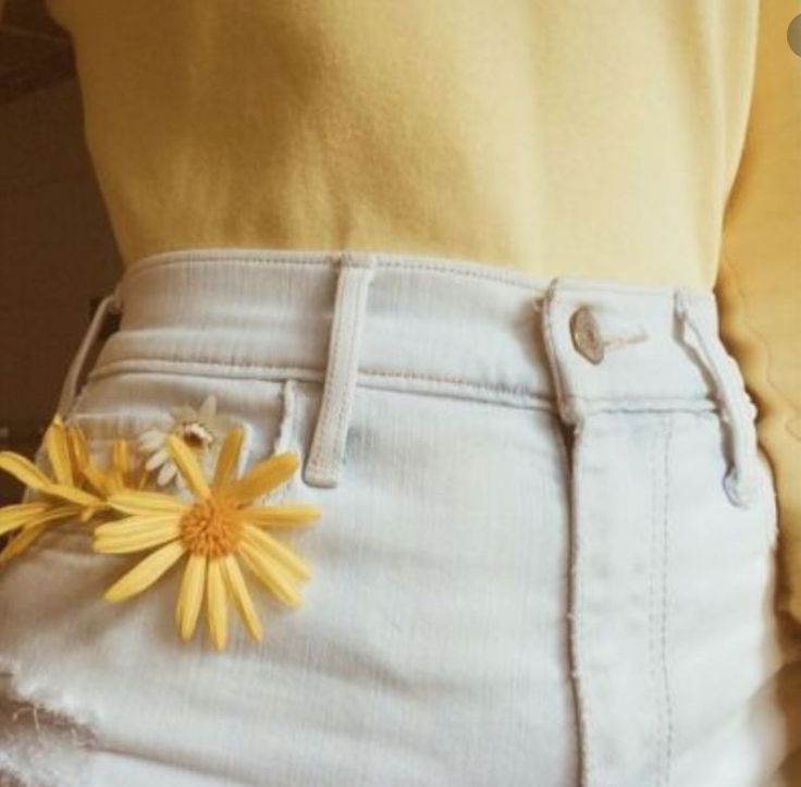 a yellow flower sticking out of the back pocket of someone's white jean shorts