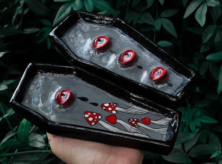 two black boxes with red hearts on them are held in front of some green leaves