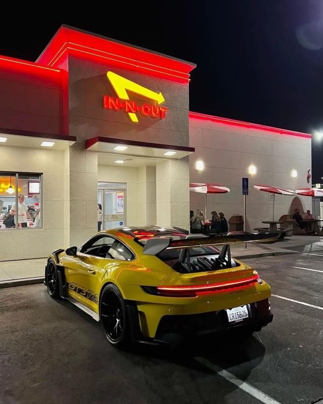 a yellow sports car is parked in front of a fast food restaurant at night time