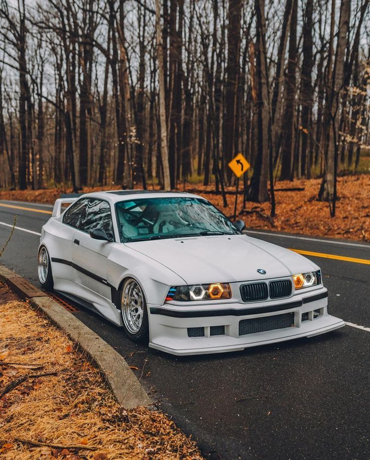 the white car is parked on the side of the road in front of some trees