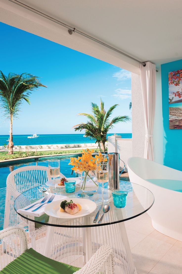 a glass table with plates and bowls on it near the water's edge in front of an ocean view