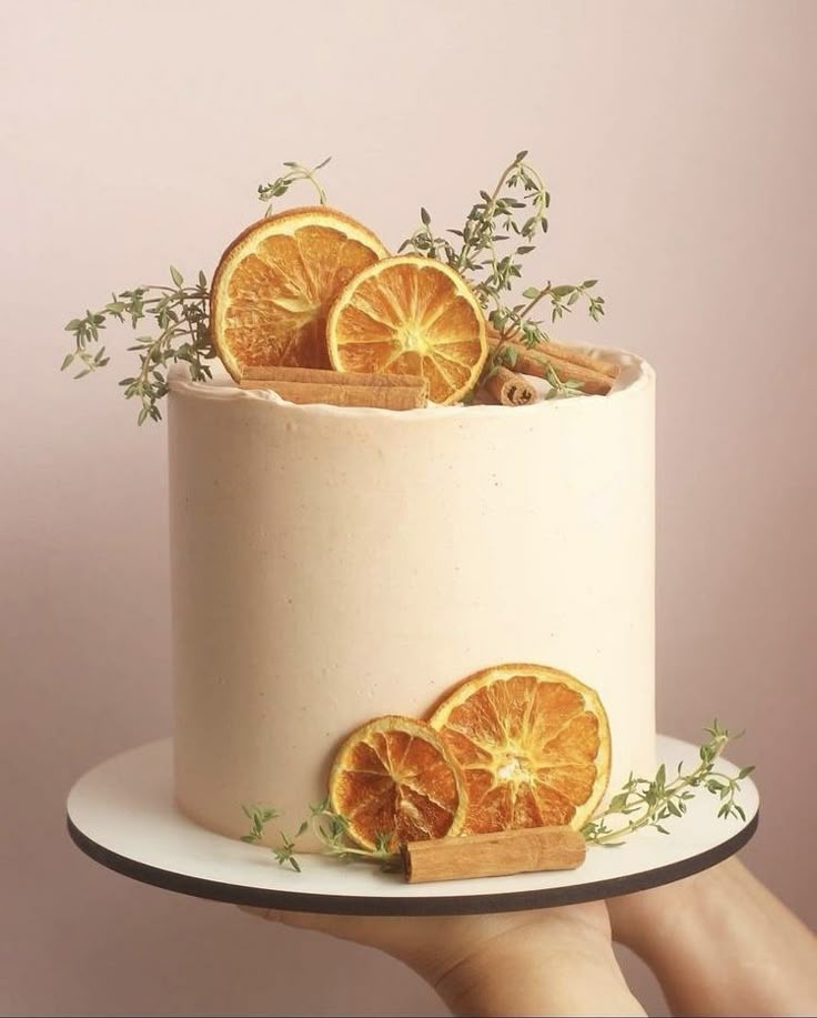 a hand holding a white cake with orange slices on it and cinnamon sticks sticking out of the top