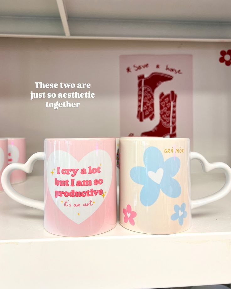 two coffee mugs sitting next to each other on top of a white shelf in a store