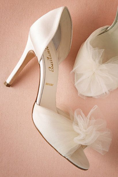 a pair of white high heel shoes next to a bride's shoe