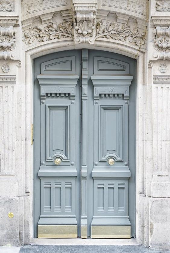 two blue doors are open on the side of a building with ornate carvings above them