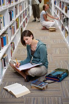 a woman sitting on the floor in a library with books and notebooks next to her