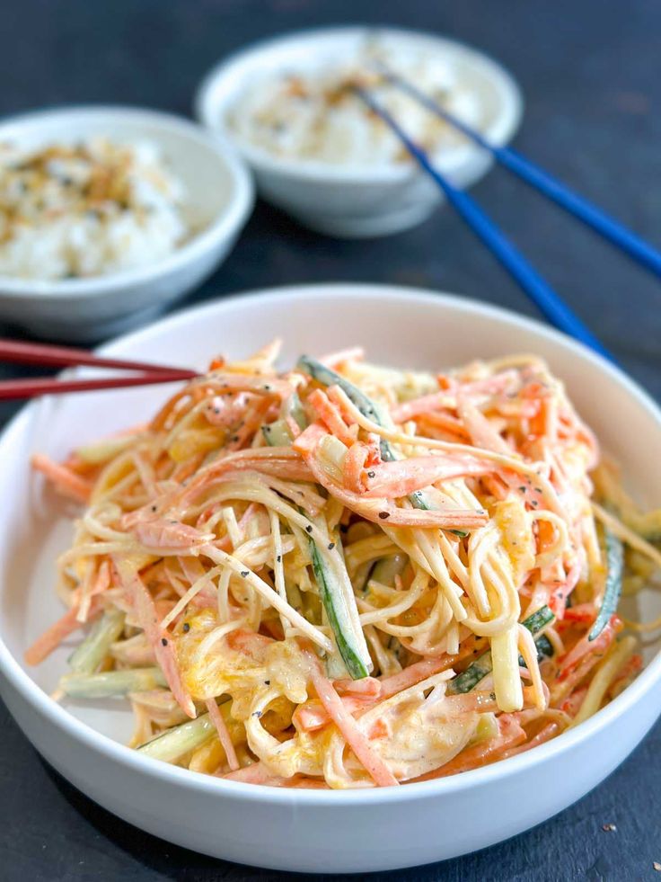 a white bowl filled with noodles and veggies next to two bowls of rice