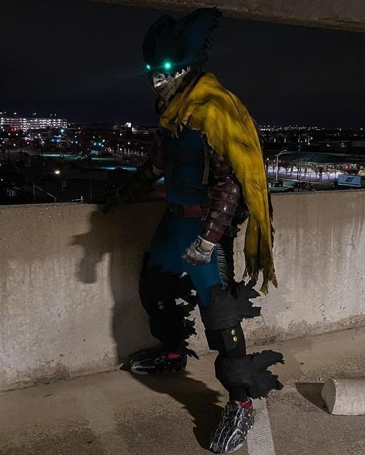 a man dressed in costume standing next to a cement wall at night with lights on