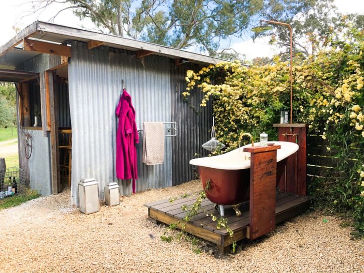 a bath tub sitting in the middle of a garden next to a shed with yellow flowers