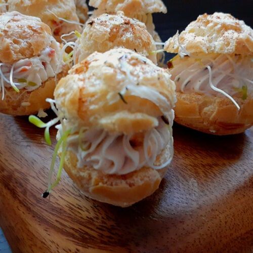 several small pastries are sitting on a wooden table with sprouts and shredded cheese