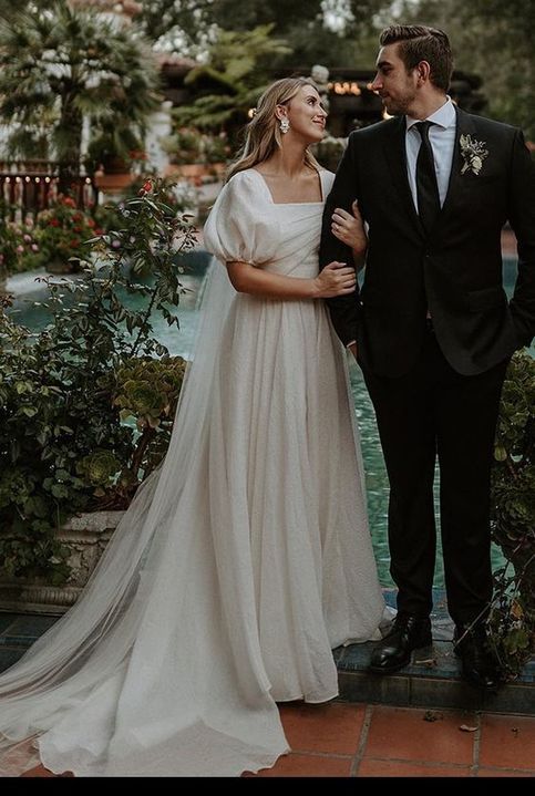 a man and woman standing next to each other in front of a fountain wearing wedding gowns