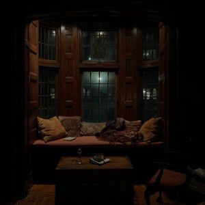 a dark room with a couch, table and window in the corner that is lit up