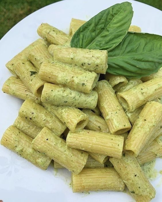 a white plate topped with pasta covered in pesto sauce and garnished with a green leaf