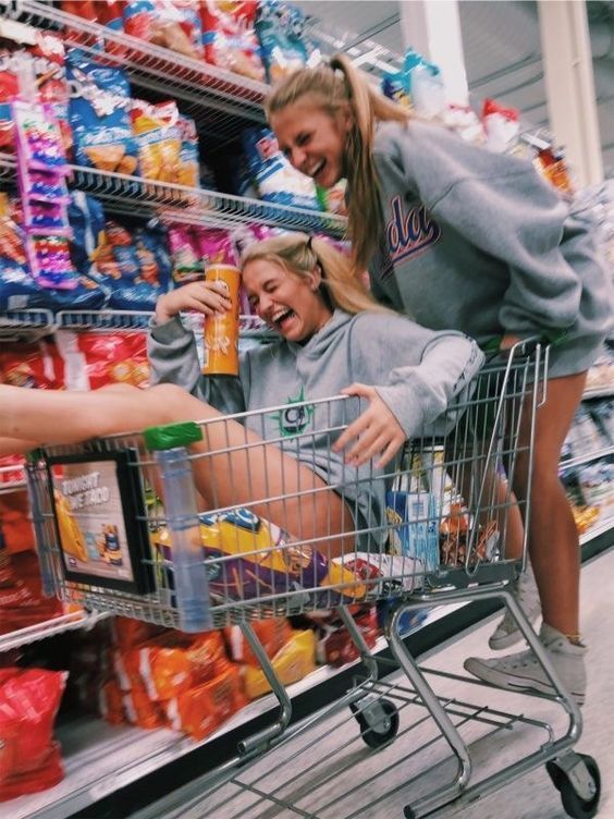 two women in grey sweatshirts pushing a shopping cart through a grocery store filled with food