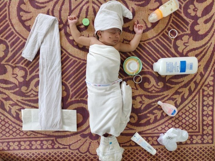 a baby wrapped in a towel laying on top of a rug next to other items