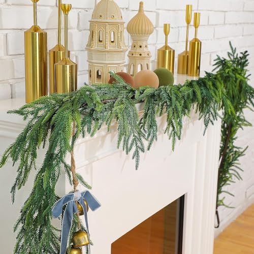 a christmas mantle decorated with evergreen branches and bells, gold candlesticks and ornaments