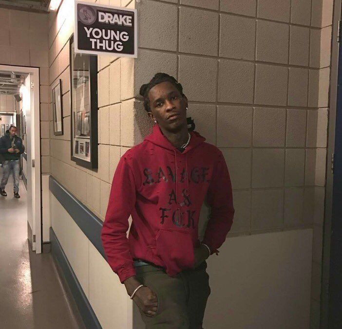 a man in a red hoodie standing next to a sign that says young thug