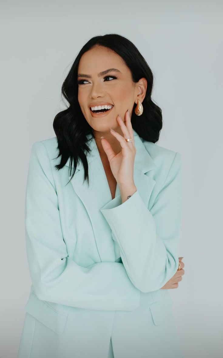 a woman in a blue suit smiling and looking at the camera with her hands on her face