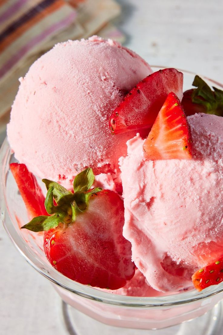 two scoops of strawberry ice cream in a glass bowl with strawberries on top