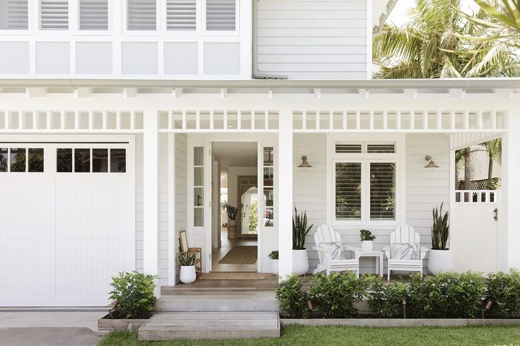 a white house with two chairs on the front porch and an entry way leading to it