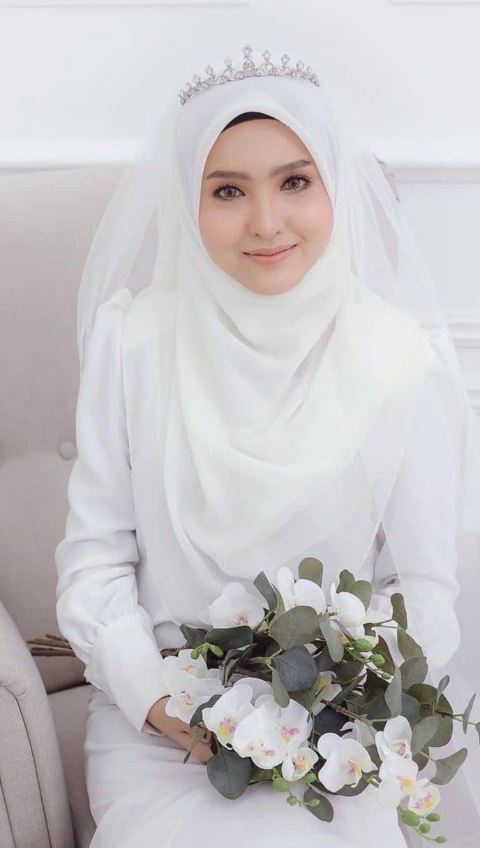 a woman wearing a white hijab and holding a bouquet of flowers in her hands