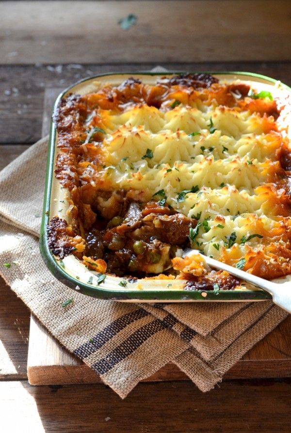 a casserole dish with meat and vegetables in it on a wooden table next to a spoon