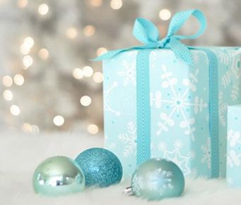 a blue gift box sitting on top of a white blanket next to two ornaments and a christmas tree