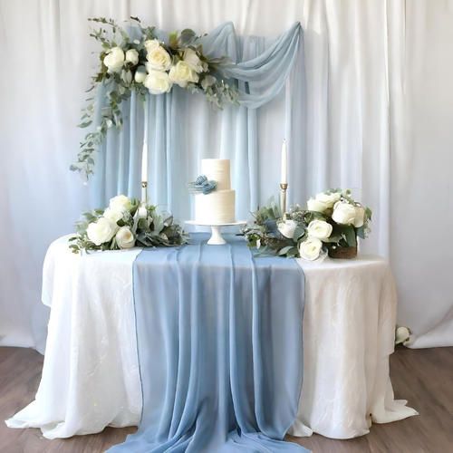 the table is decorated with white flowers and blue draping, along with a cake