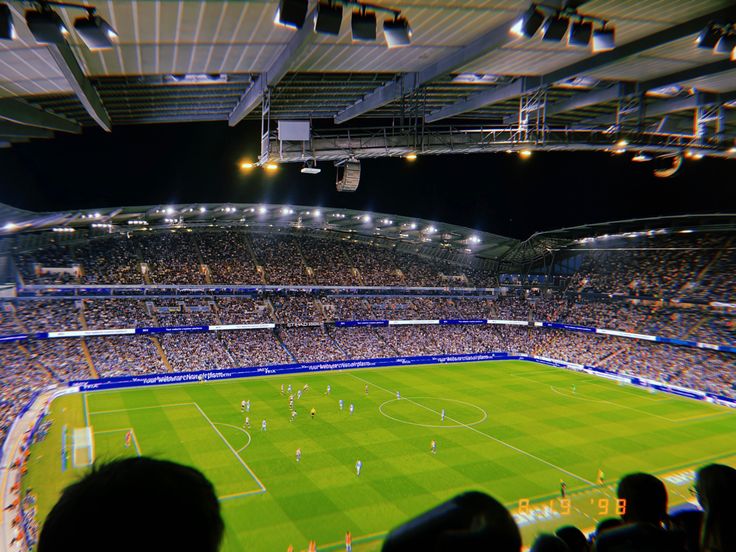 a large stadium filled with lots of people watching a soccer game at night or onlookers