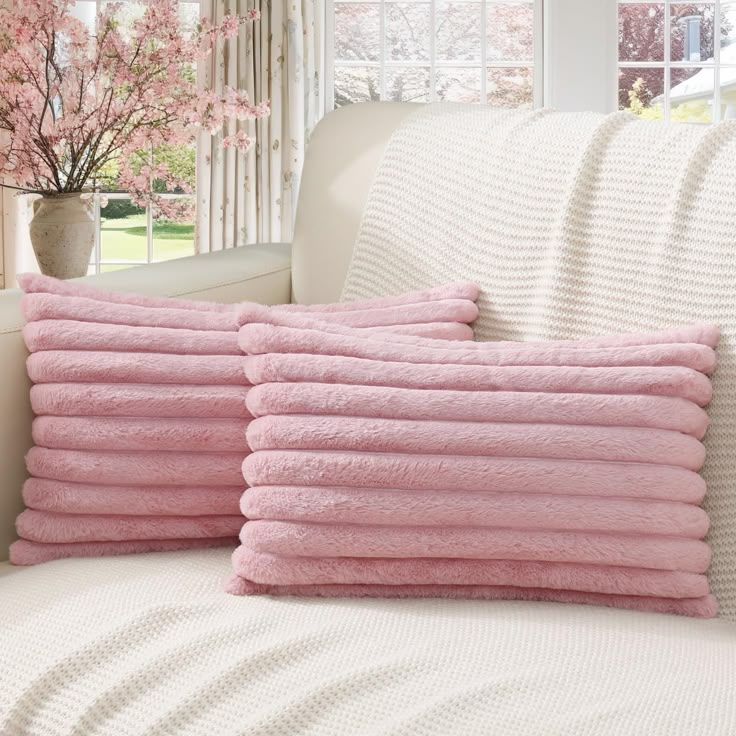 four pink towels stacked on top of each other in front of a white couch and window