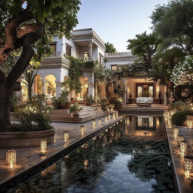 an outdoor pool surrounded by potted plants and lit candles in front of a large house