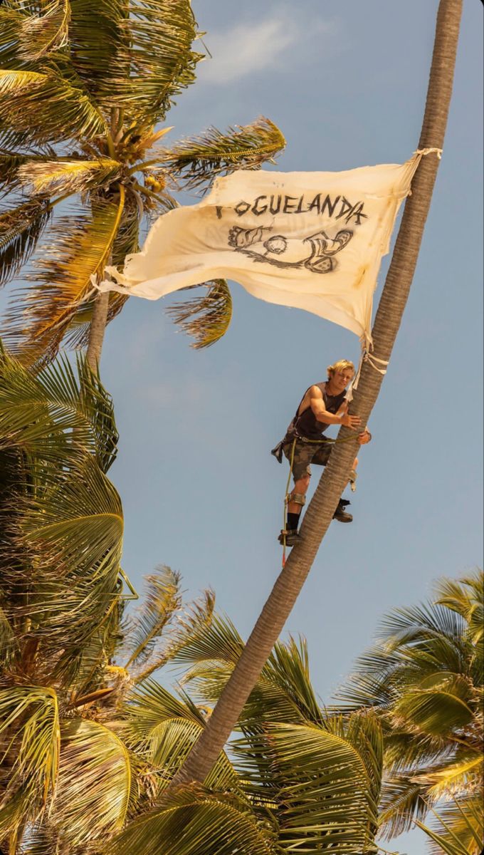 a man climbing up the side of a palm tree on top of a white flag