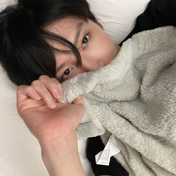 a woman laying on top of a bed covered in a blanket and looking at the camera