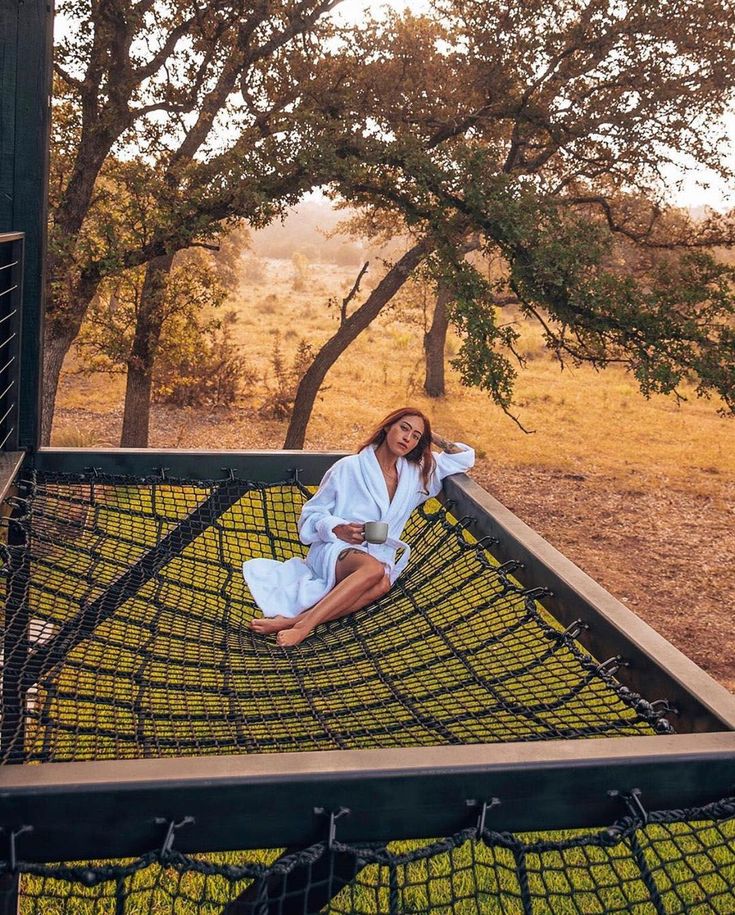 a woman sitting on top of a hammock in the middle of a field