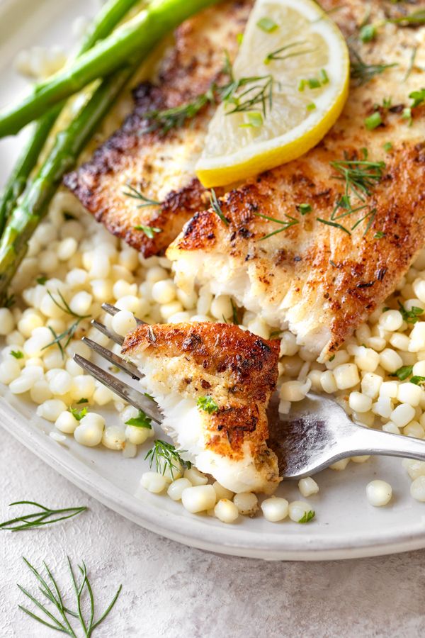 a white plate topped with chicken, corn and asparagus next to a lemon wedge