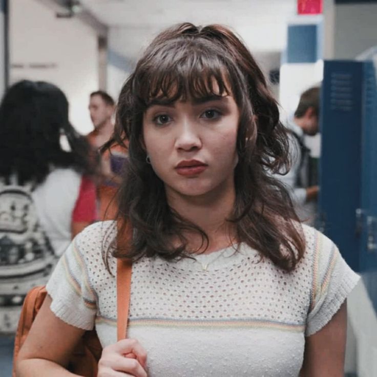 a young woman holding a book in her hand and looking at the camera while standing next to other people