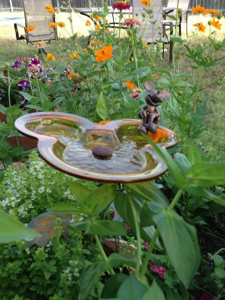 a bird bath sitting in the middle of a garden filled with lots of plants and flowers