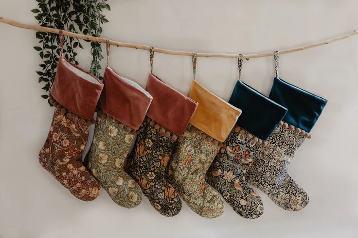 five christmas stockings hanging on a clothes line with green plants in the background and brown, red, yellow, blue, and white stocking