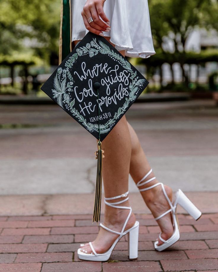 a woman in white high heels holding a black graduation cap that says, where god puts his progress