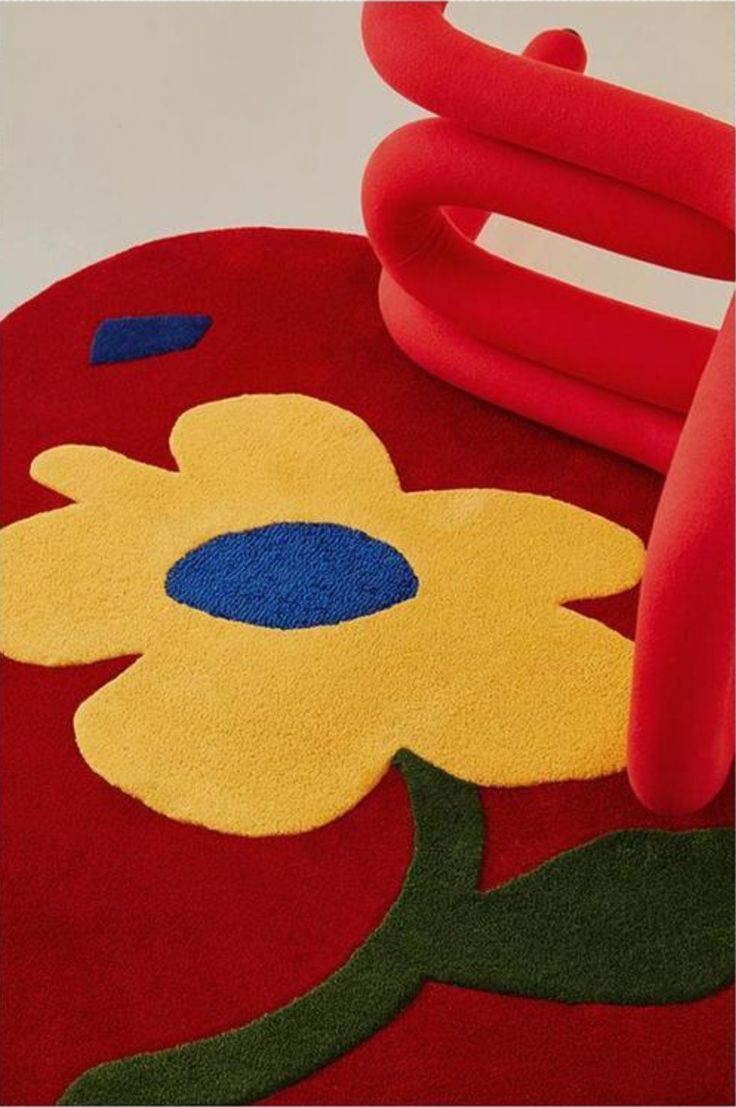 a red rug with yellow and blue flowers on the floor next to an orange chair