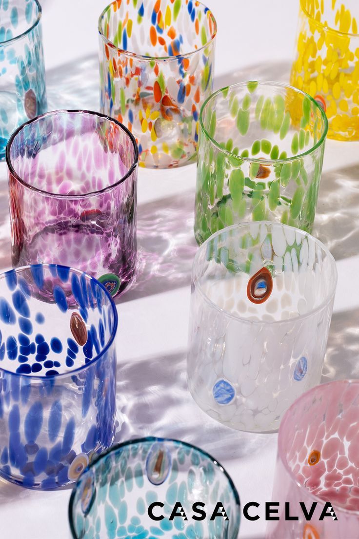 many different colored glass cups sitting on top of a white table with shadows behind them